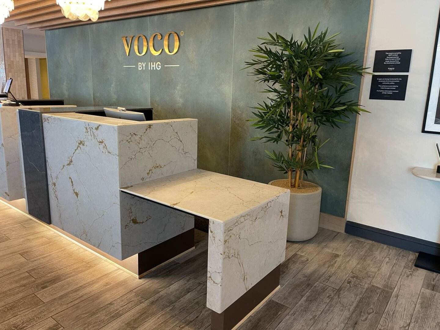 Finished voco Southampton reception desk in Silestone Versailles Ivory and Parisien Bleu quartz, with gold voco by IHG signage on a Laminam Verderame feature wall